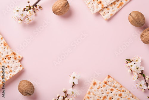 Passover celebration concept. Matzah, red kosher wine, walnut and spring beautiful branch of full bloom cherry or apple. Traditional Jewish bread on light pink background. Pesach Jewish holiday.