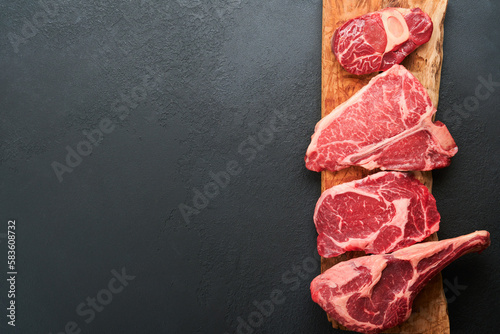 Raw prime steaks. Variety of fresh black angus prime meat steaks T-bone, New York, Ribeye, Striploin, Tomahawk cutting board on black or dark background. Set of various classic steaks. Top view.