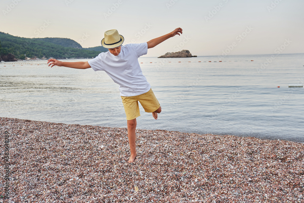 Stylish teenager walks along the pebbly seashore. The concept of summer vacation and travel.