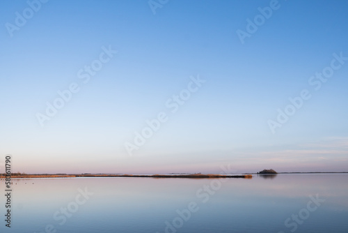 Thin strip of land peninsula surrounded by a cloudless blue sky and calm blue water