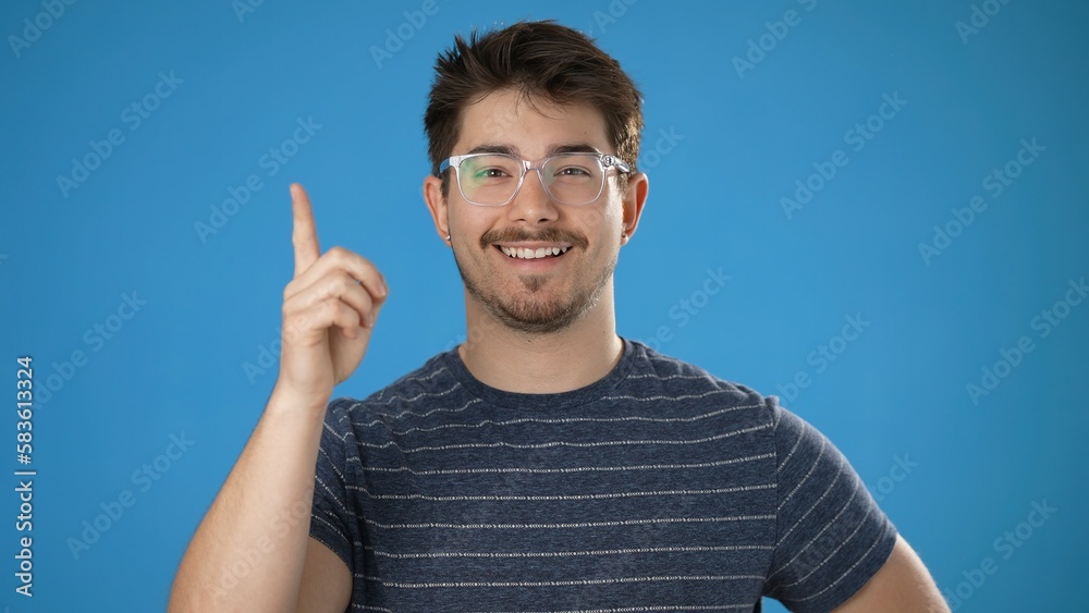 Portrait of thinking, smart puzzled pensive young hipster man 20s looks around thinks comes up with ideas raised finger isolated on plain blue background studio portrait Portrait of thinking, smart puzzled pensive young hipster man 20s looks around thinks comes up with ideas raised finger isolated on plain blue background studio portrait