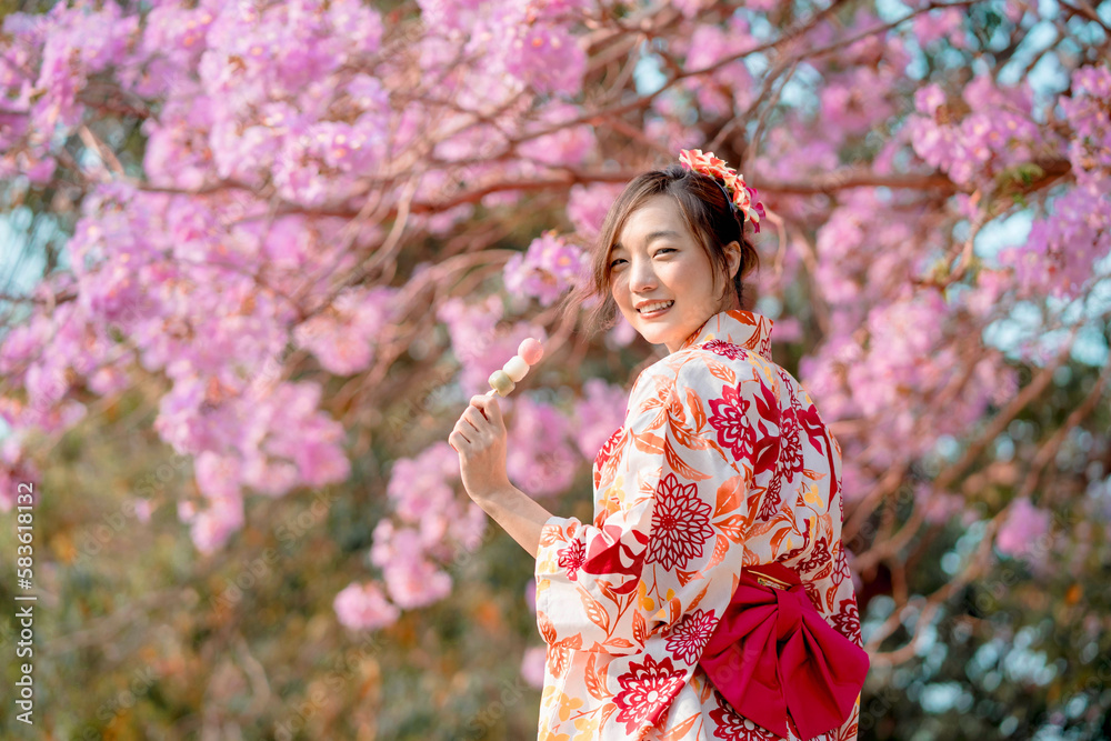 Asian woman wearing kimono costume and holding dango with cherry blossoms Asian woman wearing kimono costume and holding dango with cherry blossoms