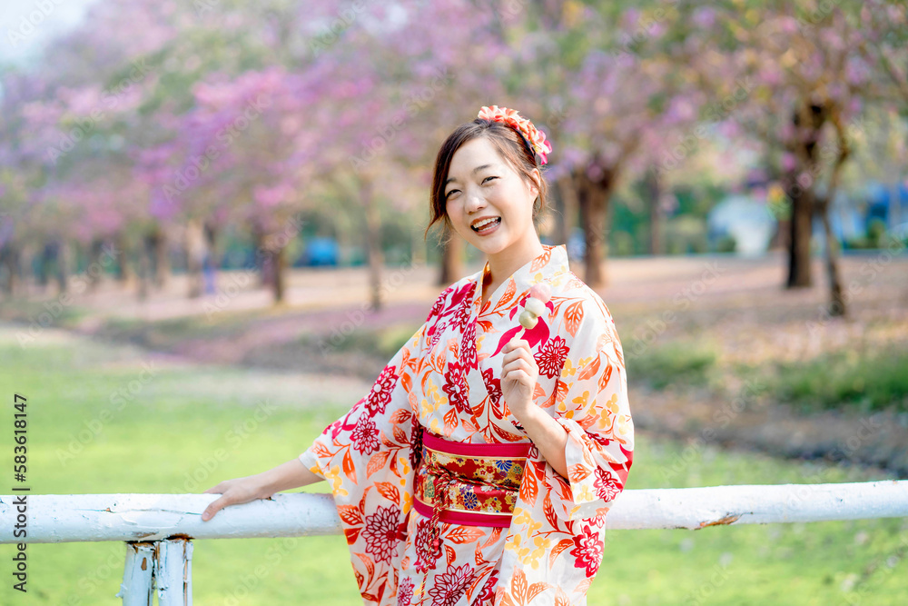Happy young woman in traditional kimono dress holding dango at bridge in spring festival. Emotion smile Happy young woman in traditional kimono dress holding dango at bridge in spring festival. Emotion smile