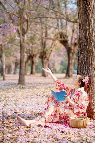 Photography lady in traditional kimono dress holding book and looking cherry blossom in spring festival