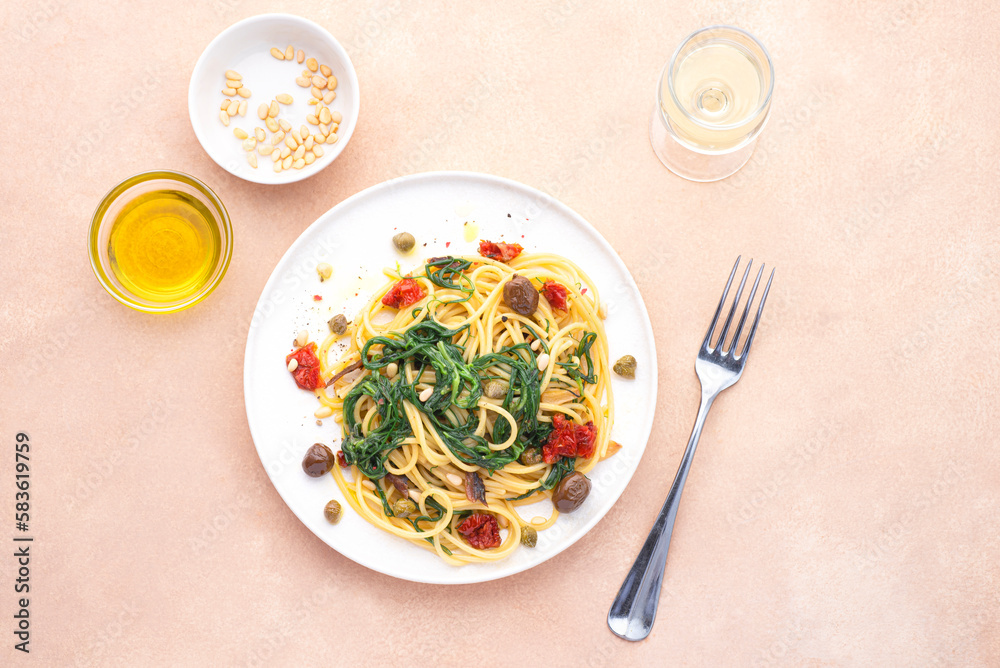 Spaghetti  with Italian Agretti, Barba di frate or Saltwort or  Salsola Soda, olives, anchovy, tomatoes, capers,  pine nuts and olive oil, spring Italian recipes. Pink soft spring background