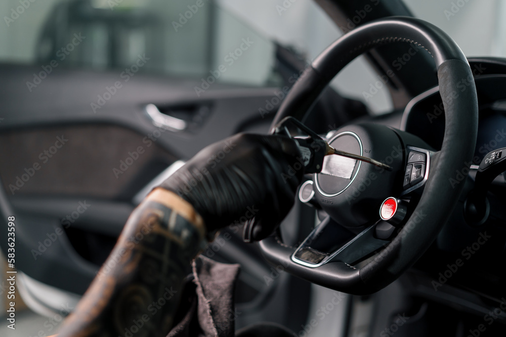 A mechanic in gloves cleans the steering wheel with a microfiber cloth and blows dust with a special tool
