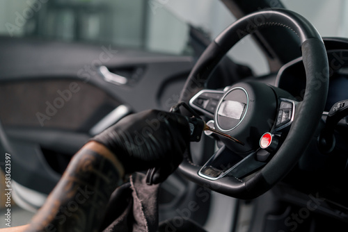 A mechanic in gloves cleans the steering wheel with a microfiber cloth and blows dust with a special tool © Guys Who Shoot