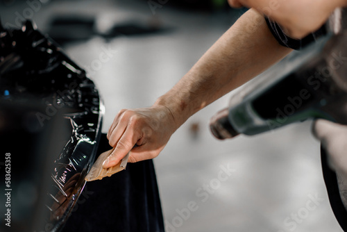 A worker covers a car spoiler with a film in the workshop using a hair dryer and a spatula close-up Car detailing and care © Guys Who Shoot