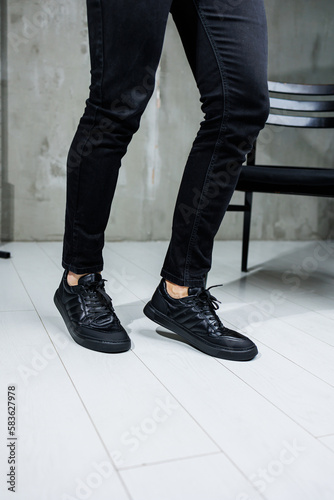 Male legs in black jeans close-up in black leather casual sneakers. Comfortable men's demi-season shoes