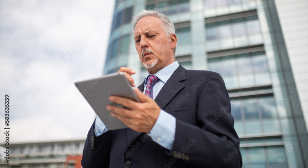 Senior businessman using his tablet in a city Senior businessman using his tablet in a city