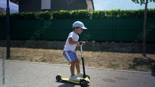 Active kid riding toy scooter outside in new urban green pathway