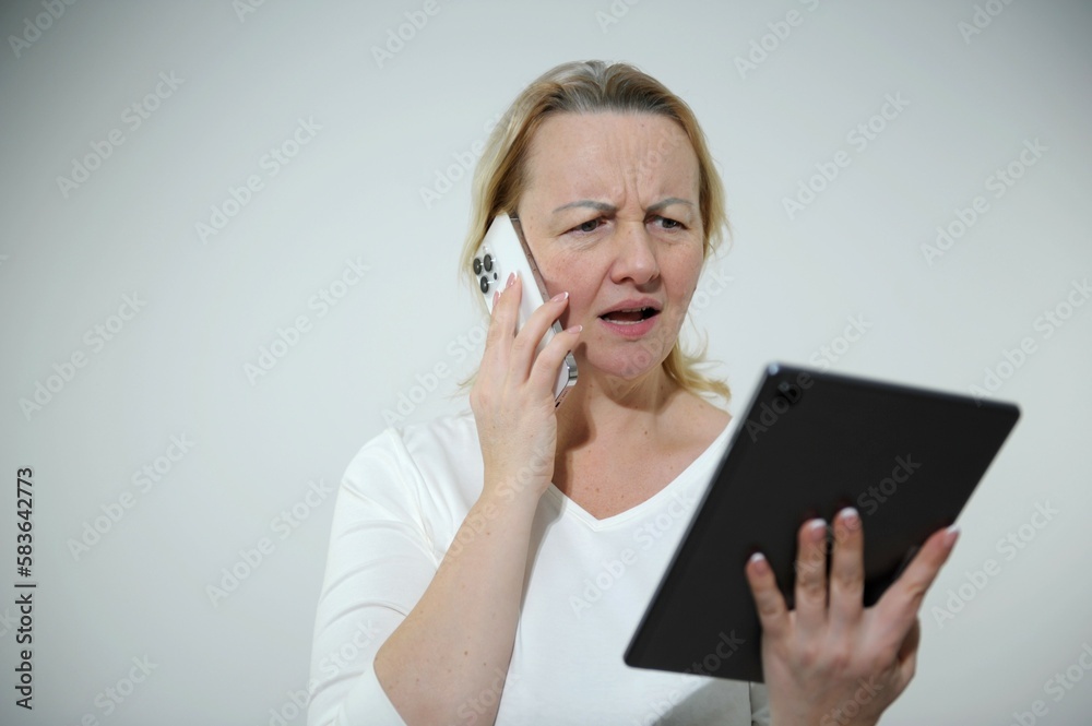 woman Seriously tense and annoyed she is standing on white background talking on phone looking at tablet she does not like woman Seriously tense and annoyed she is standing on white background talking on phone looking at tablet she does not like