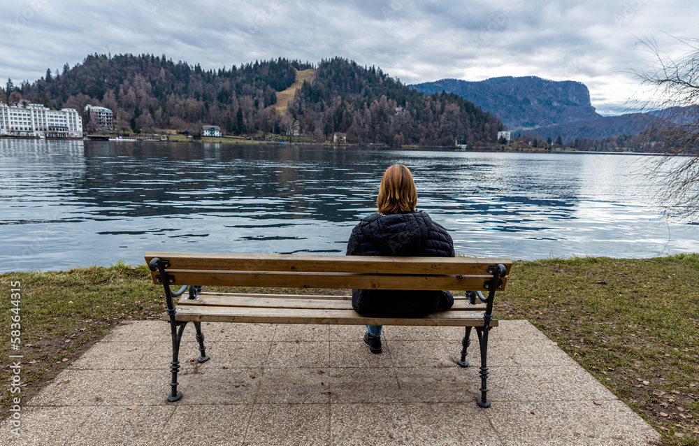 A girl sitting alone on a bench on the shore of the Slovenian Lake Bled in winter