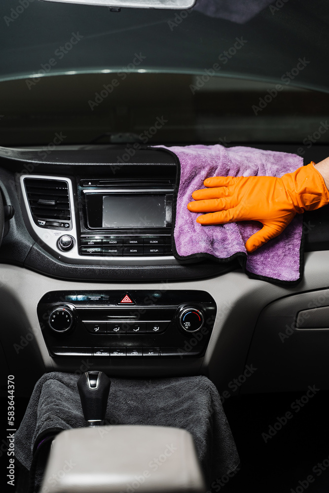 Worker in an auto detailing service is using microfiber cloth to manually dry the interior of car, specifically the dashboard area.