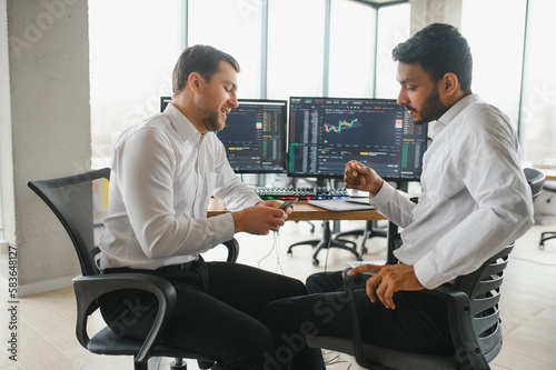 Two successful trader in formalwear pointing at display  analyzing stat and dynamic on forex charts  working in office together