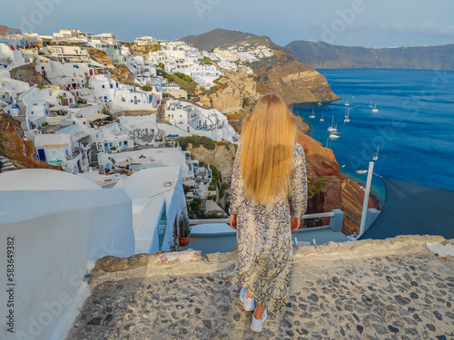 Girl with a dress standing in front of Oia village in Santorini, Greece. Picturesque view of traditional Santorini houses on the edge of the island