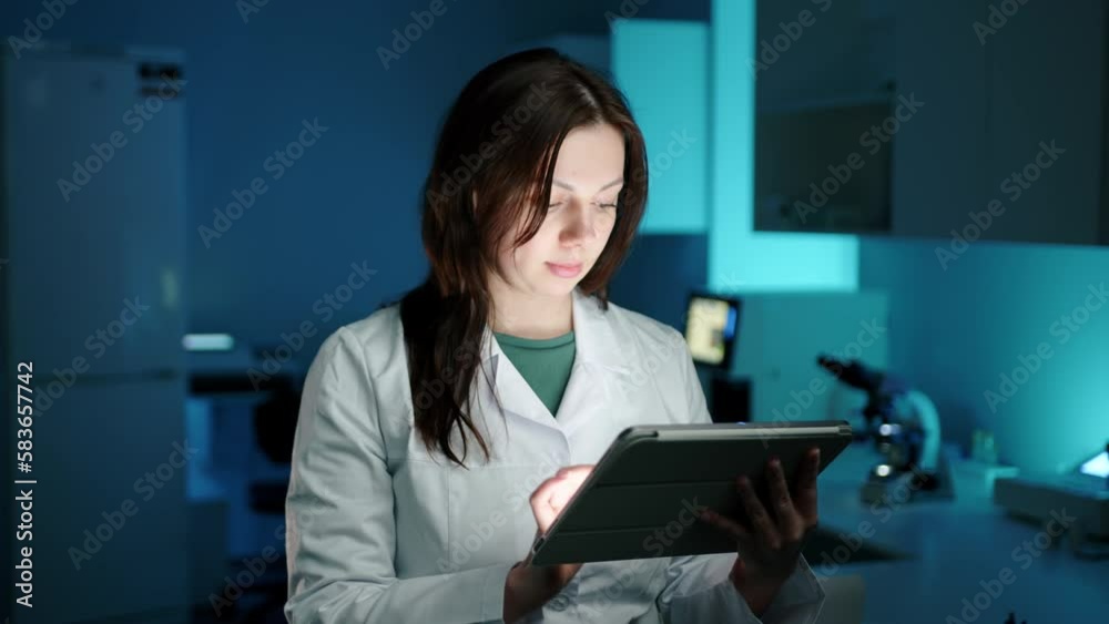 A female doctor in a dark laboratory working on something on a tablet computer. She is in a laboratory and looks focused on her work. High quality 4k footage A female doctor in a dark laboratory working on something on a tablet computer. She is in a laboratory and looks focused on her work. High quality 4k footage