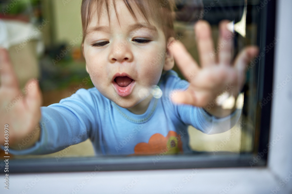 Cute little child, blond toddler boy sitting indoors looking through window