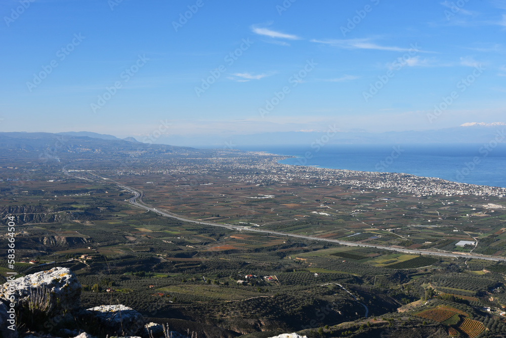 Sea and coastline view from a mountain top of ancient Acrocorinth fortress. A look from above on historic Korinthos bay, Mediterranean beach towns, olive groves, roads curves. Greece, The Peloponnese.
