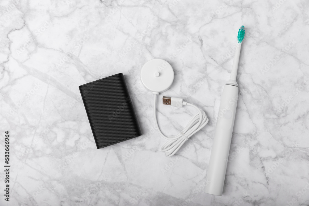 A modern electric toothbrush is charged from an external power bank battery on a marble background. Smart electric toothbrush on a pink background.Modern technologies for health. Healthy teeth. 
