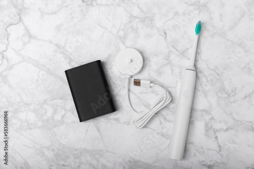 A modern electric toothbrush is charged from an external power bank battery on a marble background. Smart electric toothbrush on a pink background.Modern technologies for health. Healthy teeth.  photo
