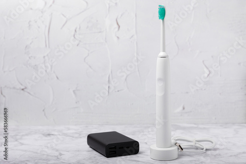 A modern electric toothbrush is charged from an external power bank battery on a marble background. Smart electric toothbrush on a pink background.Modern technologies for health. Healthy teeth. 