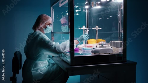 A female doctor in protective equipment putting in samples in tubes while working on a PCR cabinet. This work requires precision and careful and stady hands. High quality 4k footage  photo