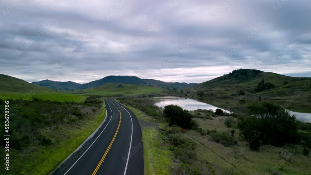 Open road through green hills and reservoir in Northern California landscape