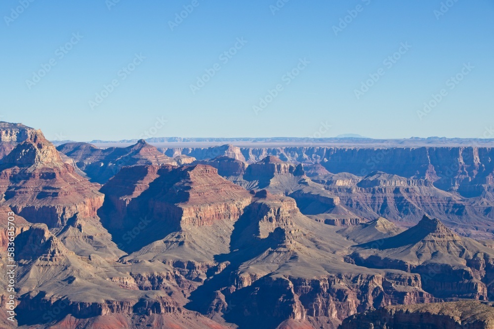 Bright desert sunlight shines down on the Grand Canyon, casting shadows on every crease and layer of the eroded canyon carved over many years by the Colorado River thousands of feet below