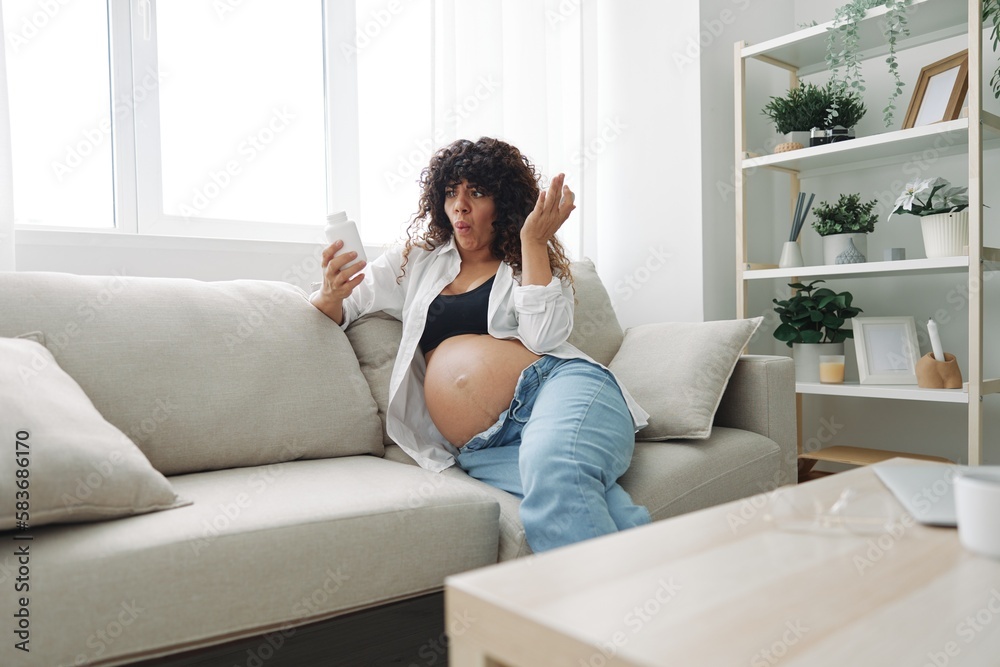 Pregnant woman surprise blogger takes vitamins and medicines sitting on the couch at home freelancer in the last month of pregnancy lifestyle before childbirth
