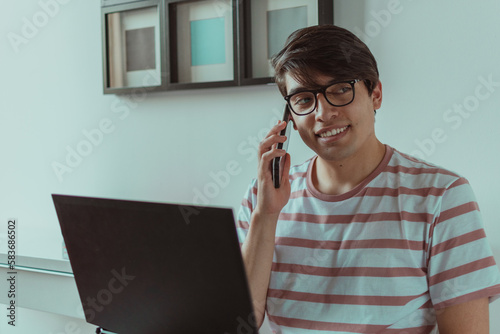 hombre joven hablando por celular en frente del laptop 