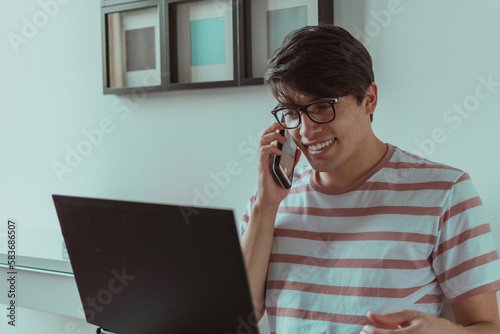 hombre joven hablando por celular en frente del laptop 