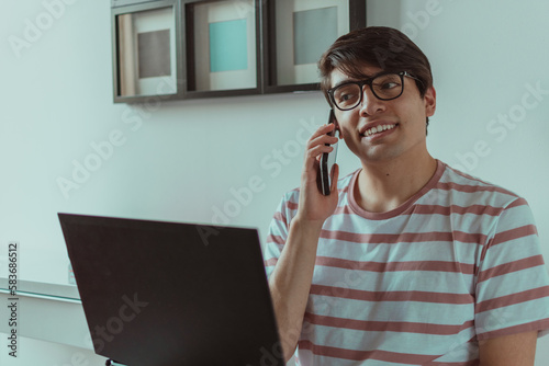 hombre joven hablando por celular en frente del laptop 