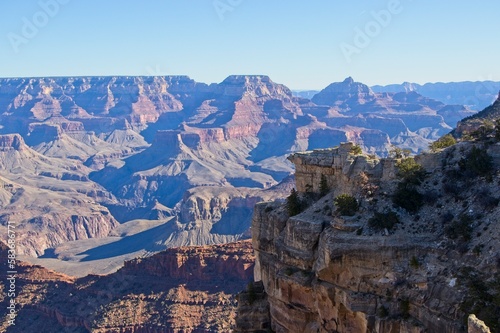 Bright desert sunlight shines down on the Grand Canyon, casting shadows on every crease and layer of the eroded canyon carved over many years by the Colorado River thousands of feet below