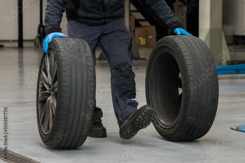 Two hands from a blue-collar worker with blue gloves rolling car tires on a gray floor in a garage workshop. car service, repair, maintenance concept. Garage workshop.