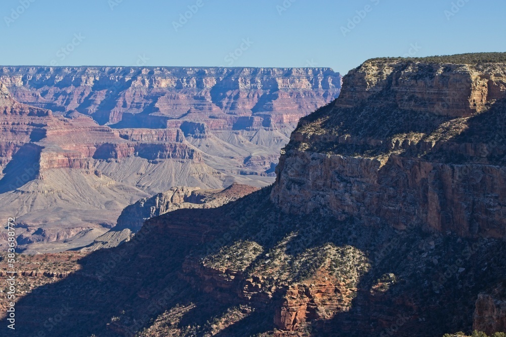 Bright desert sunlight shines down on the Grand Canyon, casting shadows on every crease and layer of the eroded canyon carved over many years by the Colorado River thousands of feet below
