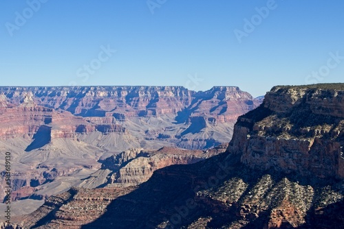 Bright desert sunlight shines down on the Grand Canyon, casting shadows on every crease and layer of the eroded canyon carved over many years by the Colorado River thousands of feet below