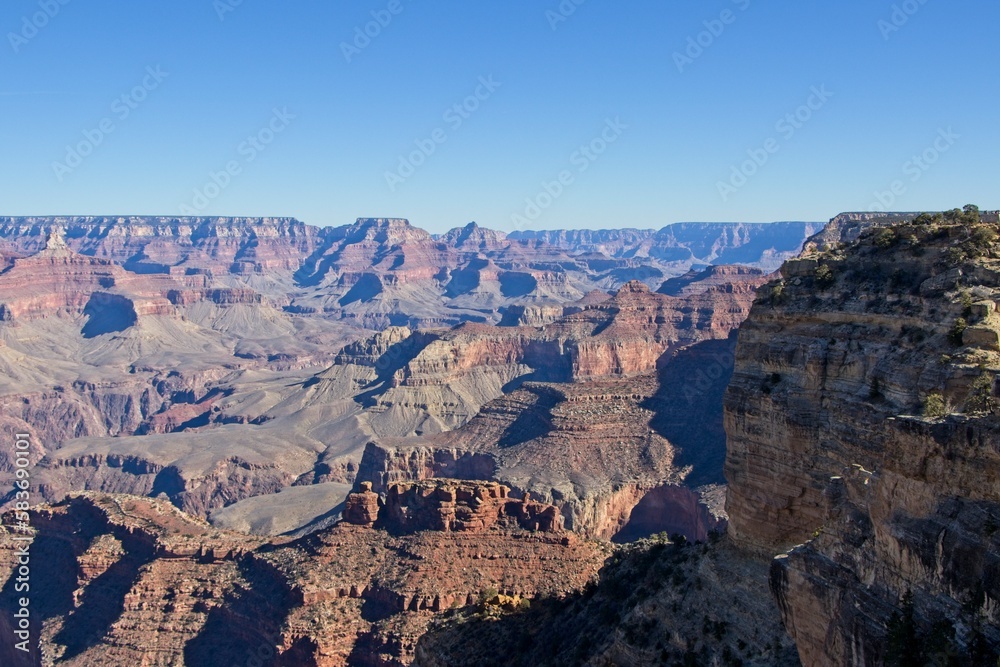 Bright desert sunlight shines down on the Grand Canyon, casting shadows on every crease and layer of the eroded canyon carved over many years by the Colorado River thousands of feet below Bright desert sunlight shines down on the Grand Canyon, casting shadows on every crease and layer of the eroded canyon carved over many years by the Colorado River thousands of feet below