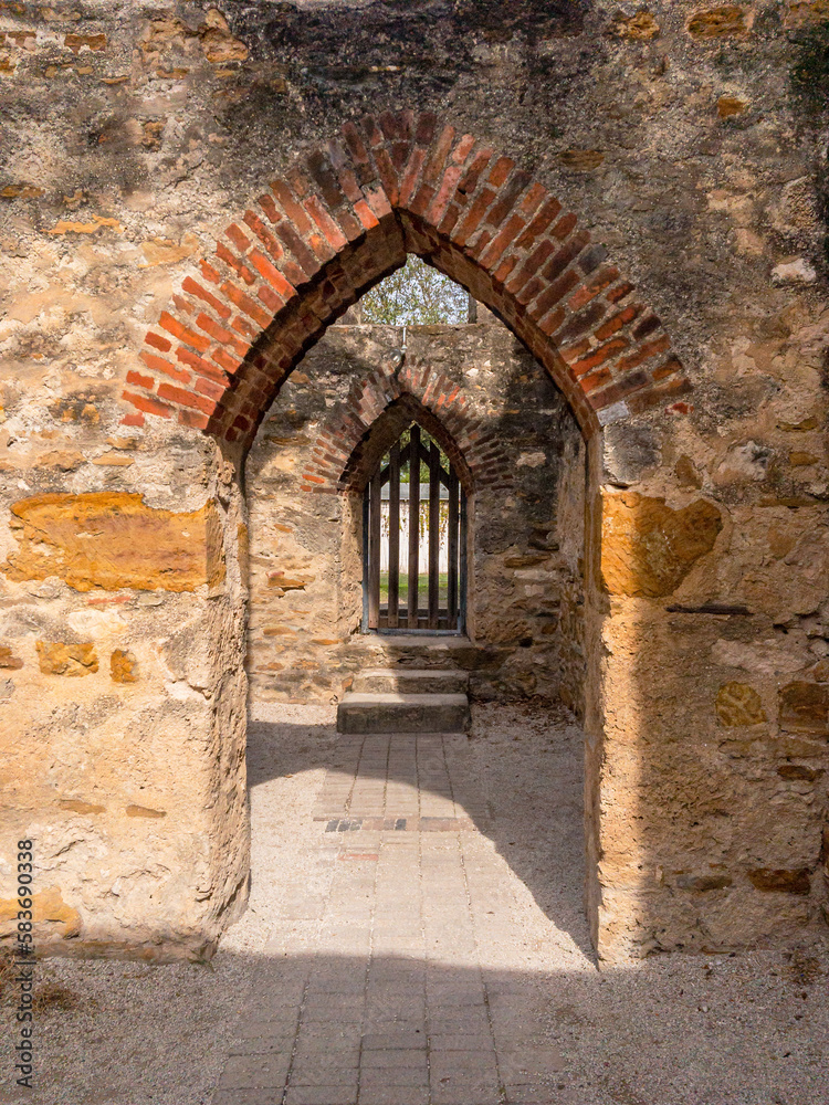 A pair of stone and brick archways - the furhter one gated - with a stone path leading through them
