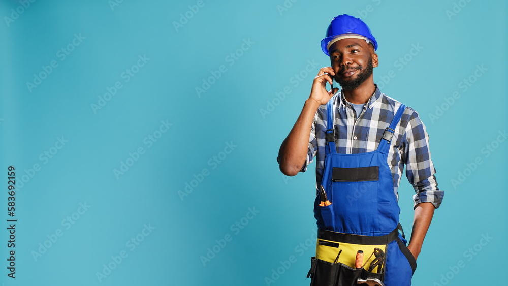 African american carpenter talking on phone call in studio, planning new construction project on camera. Male builder in overalls using smartphone line to chat remotely, building contract. African american carpenter talking on phone call in studio, planning new construction project on camera. Male builder in overalls using smartphone line to chat remotely, building contract.