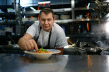 Portrait of satisfied chef placing basil leaf in plate with pasta