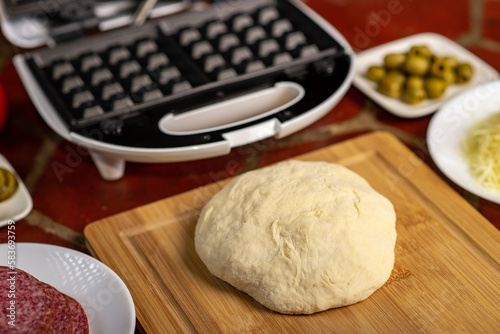 Cooking pizza waffle, piffle. Different ingredients - sausage, olives, pickles, dough on the kitchen table. photo