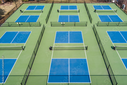 Aerial view of a new pickleball facility with blue and green courts in a suburban park in early spring.