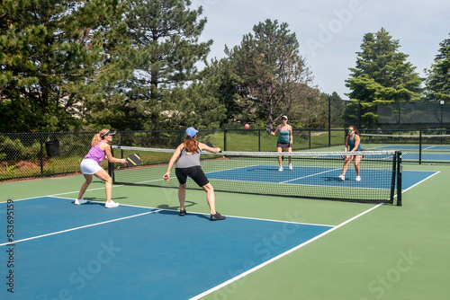 Two players approach the net in a competitive doubles game of pickleball on a blue and green court in summer.