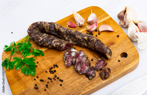 Appetizing Spanish cured pork sausage with garlic, peppercorns and a sprig of fresh parsley on a wooden chopping board. ..Close-up image