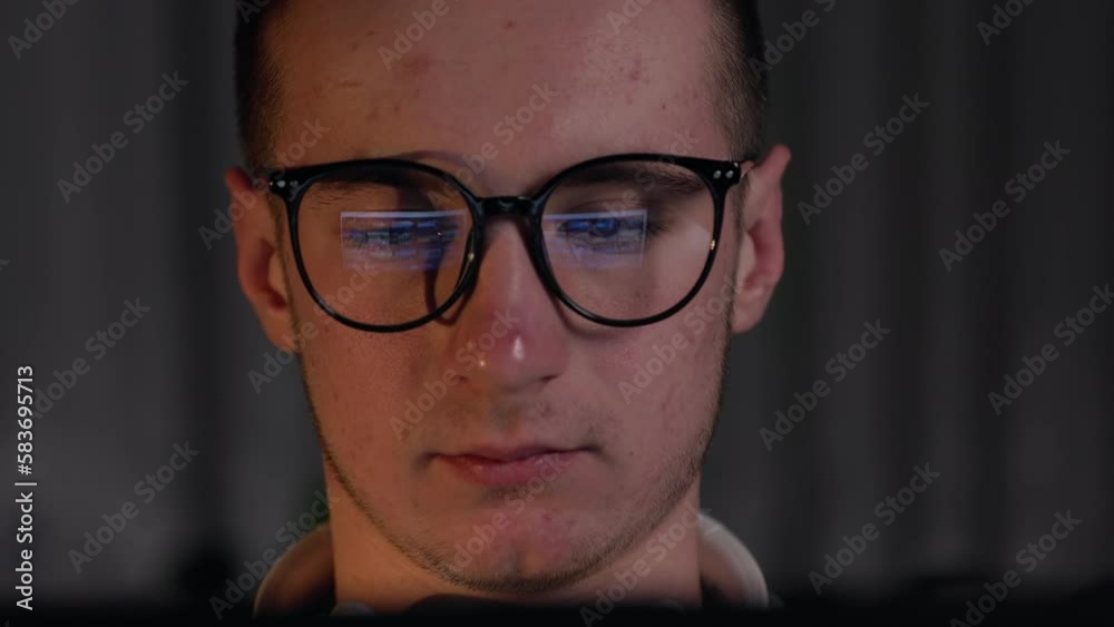 macro side view of focused man wears glasses is looking at light from the dark. Male uses pc screen, internet, TV, smartphone. Reading, watching, working online late. Copy space.