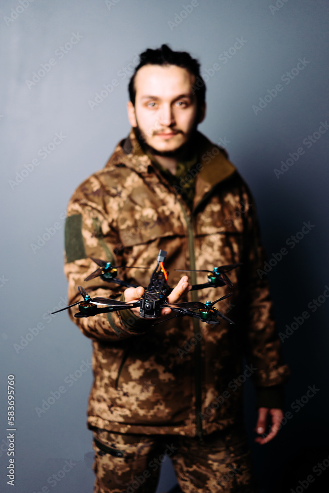 Soldier in military camouflage uniform holding fpv racing kamikaze drone bomber on blue background