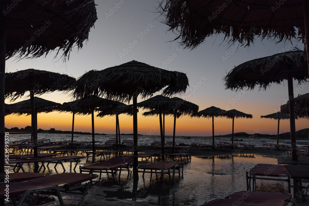 Beautiful evening scenery with sea shore, sunbeds and palm trees on the beach, Greece, Crete Beautiful evening scenery with sea shore, sunbeds and palm trees on the beach, Greece, Crete