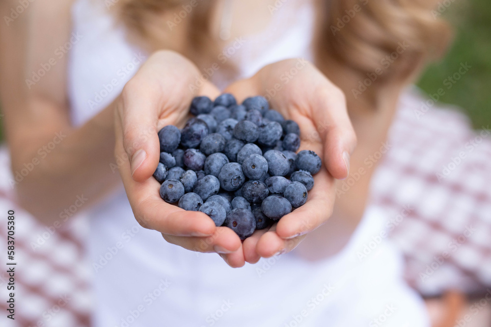 Close up photo of a caucasian woman holding a handful of ripe blueberries. This was taken in the summer. She is sitting on a red checkered table cloth. Close up photo of a caucasian woman holding a handful of ripe blueberries. This was taken in the summer. She is sitting on a red checkered table cloth.