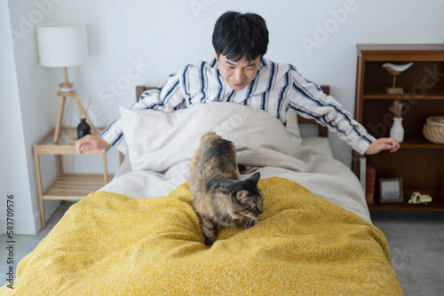 目が覚めてベッドで猫と戯れる50代男性